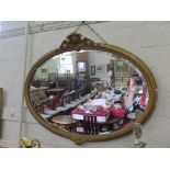 A giltwood oval wall mirror, the beaded frame with cabochon and foliate mounts, enclosing a bevelled