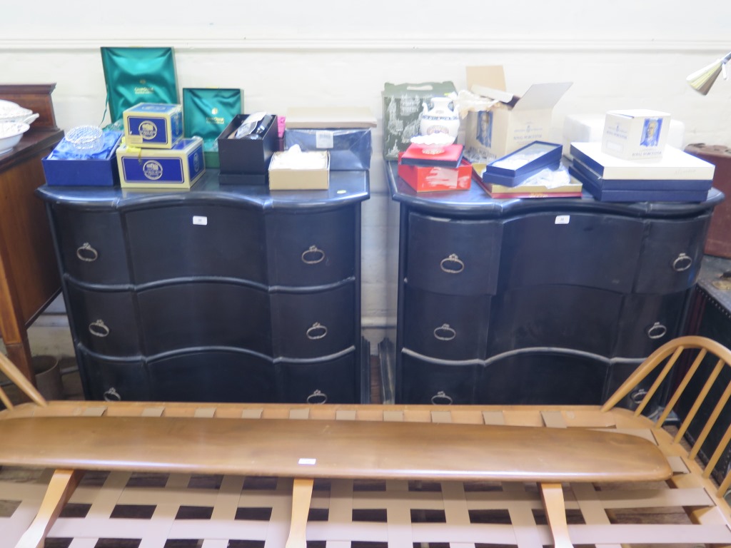 A pair of ebonised continental style chests of drawers, each with shaped fronts over three long