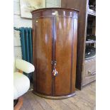 A George III oak and mahogany crossbanded bowfront hanging corner cabinet, the twin doors