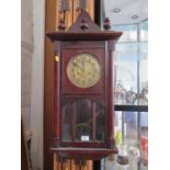 A 1920s stained beech wall clock, the finial top over a brass dial and glazed door, 80 cm high