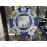 A Chinese porcelain plate, depicting a figure and a pagoda at a river, within floral panels in a