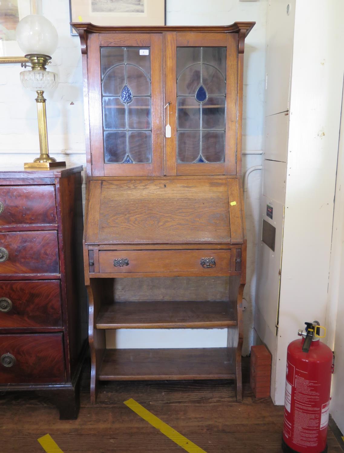 An Edwardian oak bureau bookcase, with lead glazed doors, over a sloping fall, and open shelves,