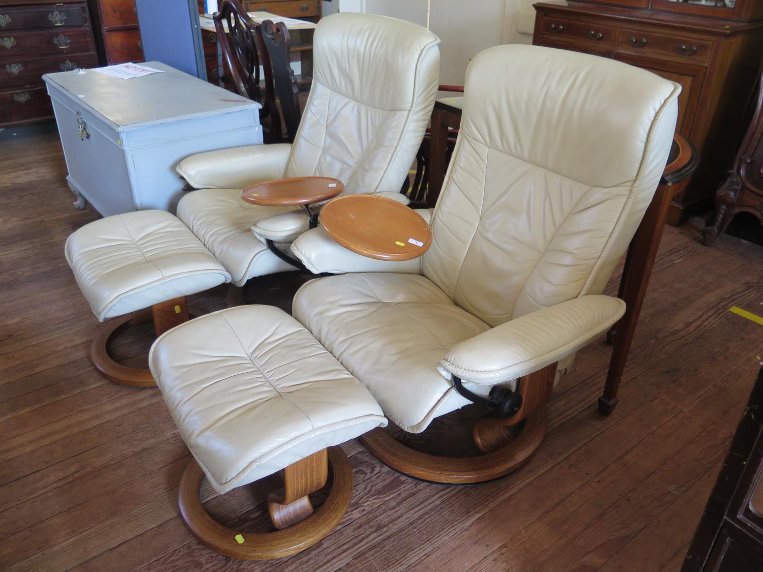 A pair of Ekornes 'Stressless' cream leather armchairs and stools, with swing tables, on circular