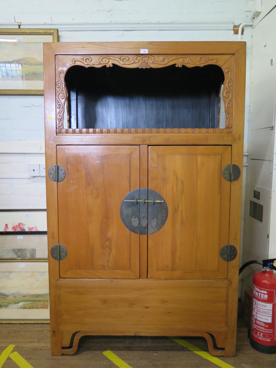 A Chinese hardwood cabinet, the open top with scroll carved frieze over of a pair of cupboard doors,