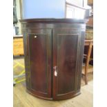 A George III mahogany bowfront corner cabinet, with dentil cornice over a pair of panelled doors