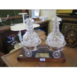 A pair of silver plated wine coasters mounted on a carriage, with two glass decanters and wine