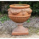 A TERRACOTTA GARDEN URN of ovoid form with ribbon tied swags of fruit and on a turned support with