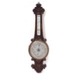 AN EDWARDIAN CARVED OAK CASED ANEROID WHEEL BAROMETER having a silvered dial and mercury tube
