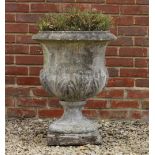A CAST RECONSTITUTED STONE GARDEN URN with flaring rim and acanthus leaf decoration on a square