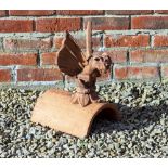 A CAST TERRACOTTA FINIAL in the form of a winged creature seated on half round ridge tile, the