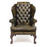 A GREEN LEATHER BUTTON UPHOLSTERED WING BACK ARMCHAIR in the Georgian style with carved cabriole