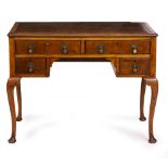A WALNUT DESK with a brown leatherette inset top, four drawers with brass drop handles and raised on