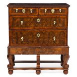 A GEORGIAN OYSTER WALNUT VENEERED CHEST ON STAND with drop handles and scrolling legs on bun feet,