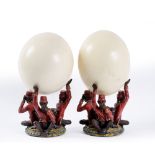 A PAIR OF OSTRICH EGGS supported by composite circus monkeys, depicting 'Hear No Evil', each 12cm