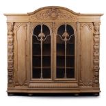 A LARGE CARVED LIGHT OAK CUPBOARD the central crest above two glazed doors, flanked by two panel