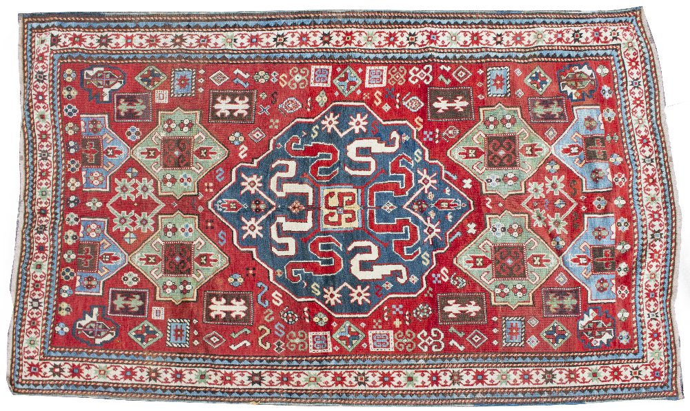 AN ORIENTAL RUG with stylised diamond shaped blue central motif to the red ground field, decorated
