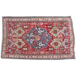 AN ORIENTAL RUG with stylised diamond shaped blue central motif to the red ground field, decorated