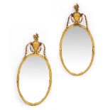 A PAIR OF NEO CLASSICAL STYLE OVAL MIRRORS with ribbon tied reeded frames surmounted by urns and