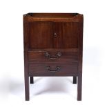 A GEORGE III MAHOGANY TRAY TOP COMMODE with pierced carrying handles, twin doors to the front and