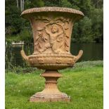 A PINK COLOURED CAST RECONSTITUTED STONE GARDEN URN of classical form decorated with putti beneath