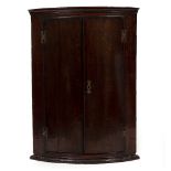 A GEORGE III BOW FRONTED HANGING CORNER CUPBOARD with carved cornice, 69cm wide x 93.5cm high