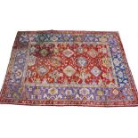 AN ANTIQUE TURKISH RED AND BLUE GROUND WOOLLEN CARPET with a banded border and geometric