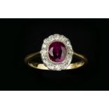 A RUBY AND DIAMOND CLUSTER RING, the oval mixed-cut ruby in millegrain collet setting, bordered by
