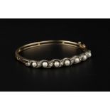 A PEARL AND DIAMOND BANGLE, of hinged oval bifurcated form, applied with an openwork scrolled