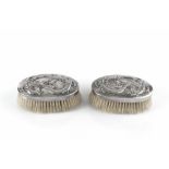 A PAIR OF EARLY 20TH CENTURY CHINESE EXPORT SILVER BACKED CLOTHES BRUSHES by Wang Hing, relief
