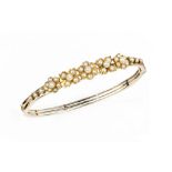 A HALF PEARL BANGLE, of hinged oval trifurcated form, applied with a frieze of half pearl set
