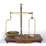 A LATE 19TH CENTURY BRASS SET OF SCALES by J.H. Heal & Co. Halifax England, standing on a mahogany