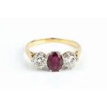 A RUBY AND DIAMOND THREE STONE RING, the oval mixed-cut ruby claw set between two round brilliant-