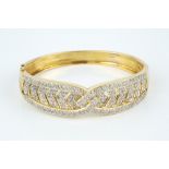A DIAMOND SET BANGLE, of hinged oval form and fluted crossover design, pavé set with channels of