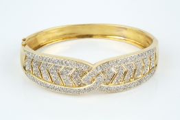 A DIAMOND SET BANGLE, of hinged oval form and fluted crossover design, pavé set with channels of