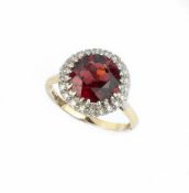 A GARNET AND DIAMOND CLUSTER RING, the circular mixed-cut garnet claw set within a border of