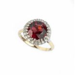 A GARNET AND DIAMOND CLUSTER RING, the circular mixed-cut garnet claw set within a border of