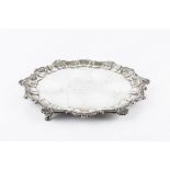 A SILVER SALVER, with shell and scroll cast border, on shaped feet, presentation inscription, by