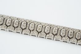 A DIAMOND SET PANEL BRACELET, designed as a line of articulated geometric panels, each millegrain
