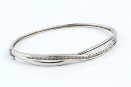 A DIAMOND SET BANGLE, of hinged oval form, set to the top with a crossover channel of single-cut