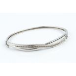 A DIAMOND SET BANGLE, of hinged oval form, set to the top with a crossover channel of single-cut