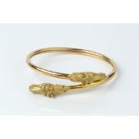 AN 18CT GOLD BANGLE, of crossover design, the horse's head terminals with red stone eyes, with
