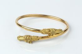 AN 18CT GOLD BANGLE, of crossover design, the horse's head terminals with red stone eyes, with