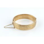 A 9CT GOLD BANGLE, of hinged oval form, with engraved decoration, hallmarked for Birmingham 1977,