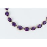 AN AMETHYST RIVIÈRE NECKLACE, comprising a line of graduated oval mixed-cut amethysts in pinched