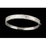 A DIAMOND BANGLE, of hinged oval form, channel set to the front with a line of baguette-cut