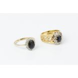 TWO SAPPHIRE AND DIAMOND CLUSTER RINGS, the first centred with an oval mixed-cut sapphire and