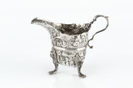 AN 18TH CENTURY IRISH SILVER CREAM JUG, the girdled body embossed and engraved with flowers and
