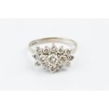 A DIAMOND CLUSTER RING, centred with a trio of round brilliant-cut diamonds, bordered by graduated