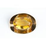 A CITRINE SINGLE STONE BROOCH, the oval mixed-cut citrine in four claw setting, to a concave oval