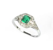 AN EMERALD AND DIAMOND PANEL RING, the octagonal step-cut emerald millegrain collet set within a